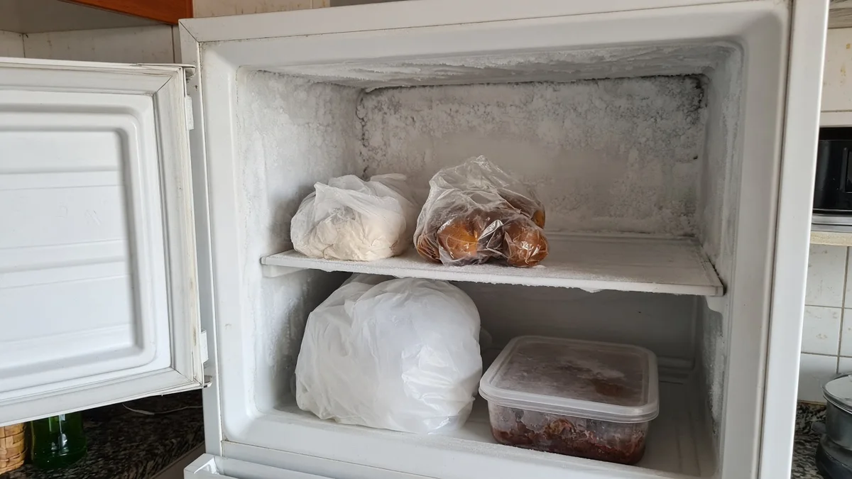 Freezer com camada fina de gelo ilustrando sistema defrost, em residência brasileira, com técnico Refrigeração Curitiba Pro e materiais e ferramentas ao lado.